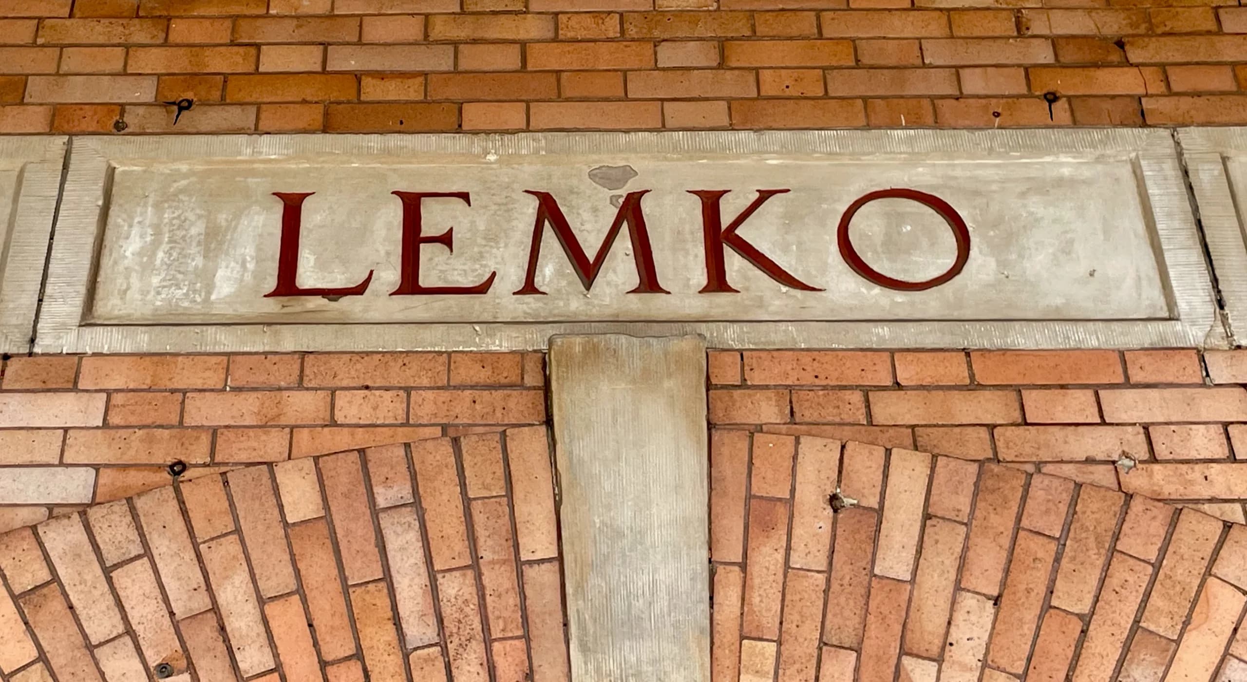 Close-up of the historic LEMKO lettering carved into stone above the building entrance, showcasing beautiful brick archwork