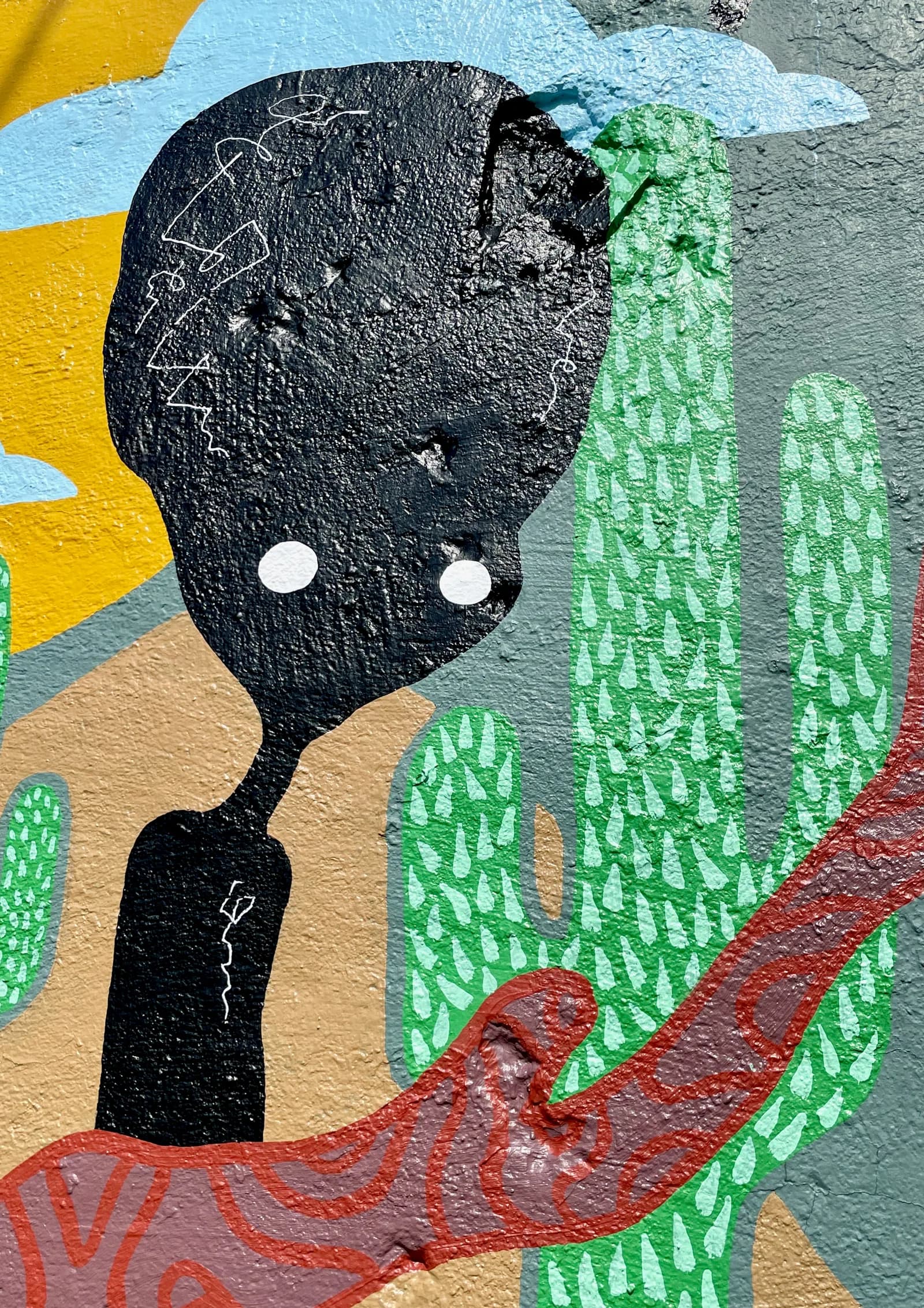 Close-up of a figure's head in the “Never Stop Searchin'” mural against the desert sun and cactuses