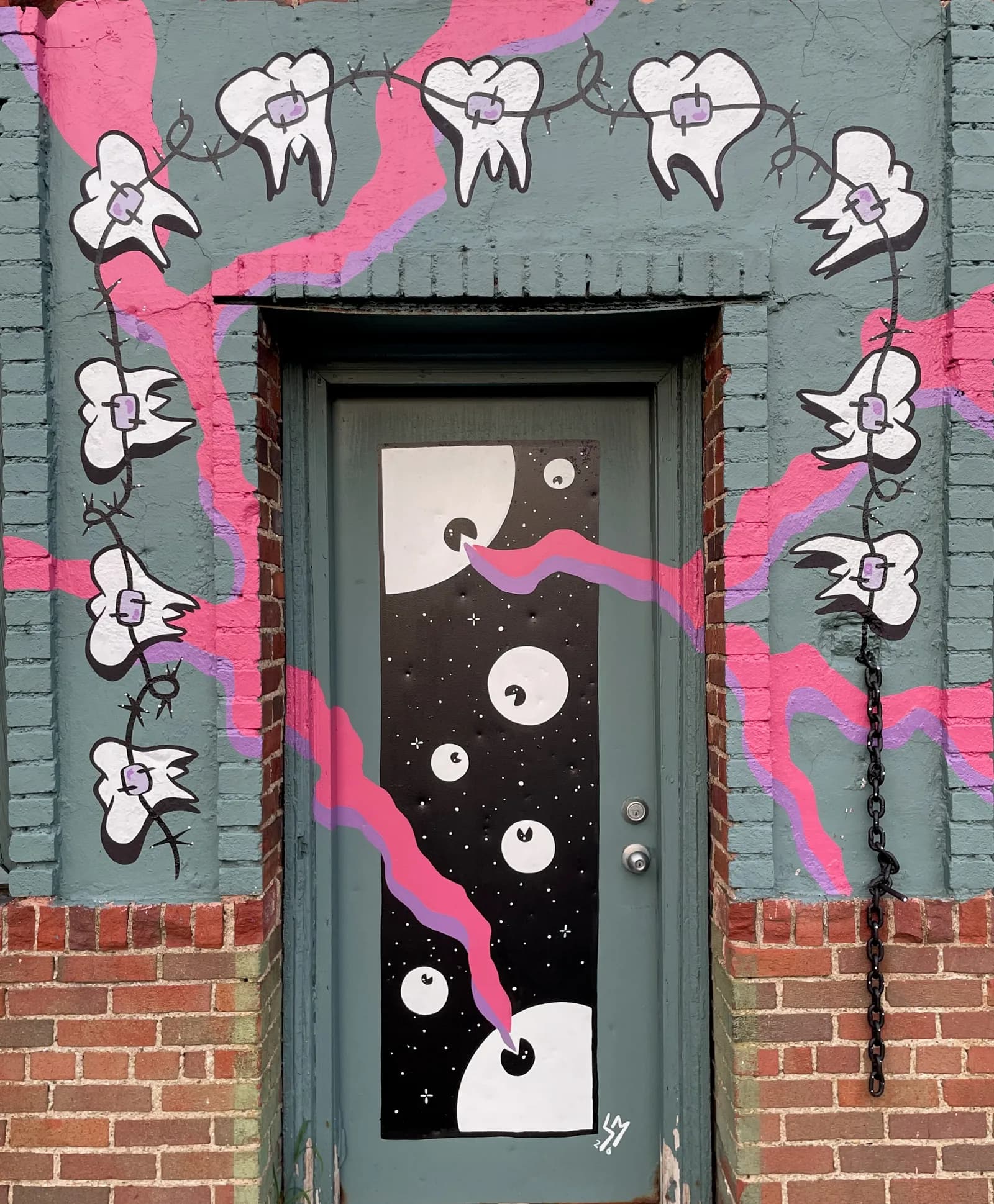 Casey Micksun's “Searchin'” door mural — a starry black panel of crescent-moon eyes framed by braces-clad teeth on pink barbed wire